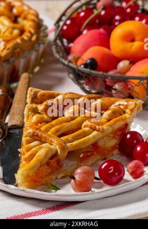 Torta di albicocche decorata con decorazioni a base di impasto e un cestino di metallo con frutta e frutti di bosco. Foto Stock