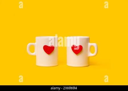 Due tazze bianche con due cuori rossi su sfondo giallo con spazio per le copie Foto Stock