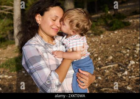 Un momento caldo e tenero di una madre che tiene e bacia suo figlio all'aperto. La scena cattura il legame tra amore, affetto e Unione Foto Stock