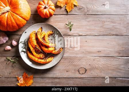 Fette di zucca arrostite con aglio ed erbe aromatiche su fondo in legno, vista dall'alto, spazio di copia. Zucca piccante al forno, contorno stagionale autunnale o grigliata Foto Stock