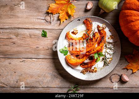 Zucca arrosto con yogurt greco, aglio ed erbe aromatiche su un tavolo di legno, vista dall'alto, spazio per copiare. Ricetta calda invernale per insalata di zucca piccante con labnea soffice goa Foto Stock