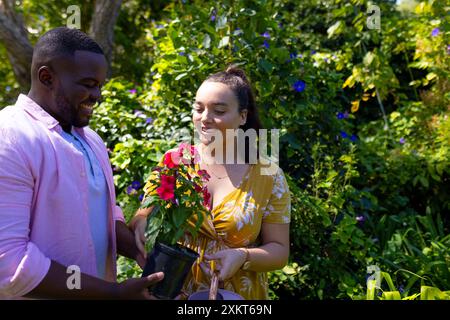 Tenere una pianta in vaso, sorridere una coppia che si diverte a giardinaggio all'aperto Foto Stock