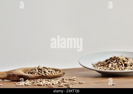 Cucchiaio di legno con porzione di semi di girasole sgusciati e piatto con un'altra porzione sul lato destro fuori fuoco. Foto Stock