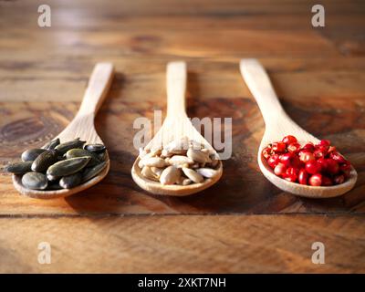 Tre cucchiai di legno ripieni di riso, pepe rosa, semi di zucca e lenticchie. Vista dall'alto Foto Stock