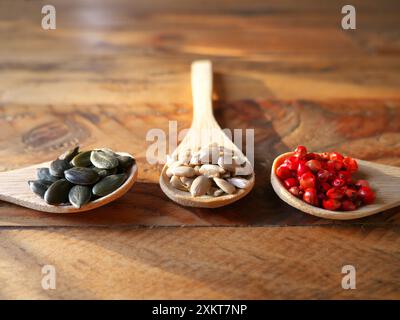 Tre cucchiai di legno ripieni di riso, pepe rosa, semi di zucca e lenticchie. Vista dall'alto Foto Stock