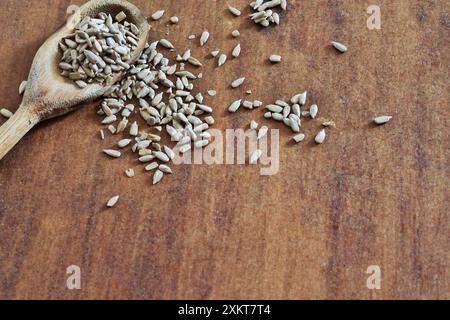 Cucchiaio di legno con porzione di semi di girasole sgusciati e semi sparsi sul tavolo fotografati dall'alto. Foto Stock