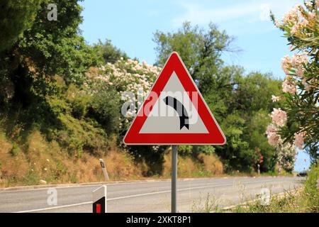 Cartello stradale pericoloso svolta a sinistra su una strada di montagna in Croazia. Strada curva, segnale stradale triangolare, triangolo bianco-rosso con freccia Foto Stock