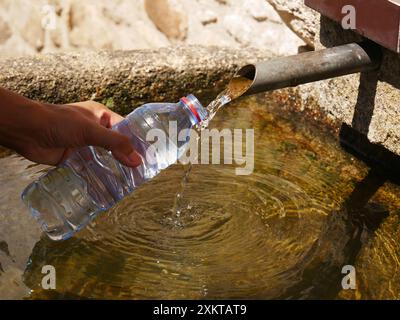 Un primo piano di una mano che tiene una bottiglia di plastica e riempendo con acqua potabile da una sorgente Foto Stock