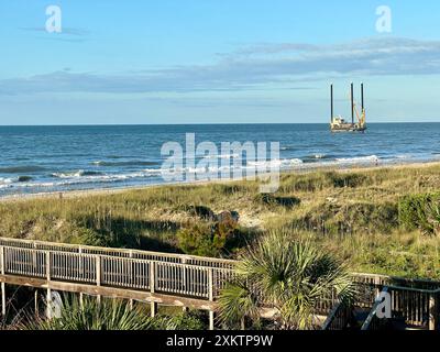 Una passerella in legno, accanto alle dune, guida i visitatori verso l'oceano durante una vacanza estiva, una draga visibile in lontananza a North Myrtle Beach. Foto Stock