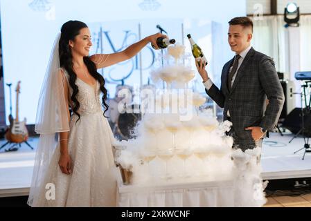 gli sposi novelli al banchetto versano champagne in una pila di bicchieri per gli ospiti Foto Stock