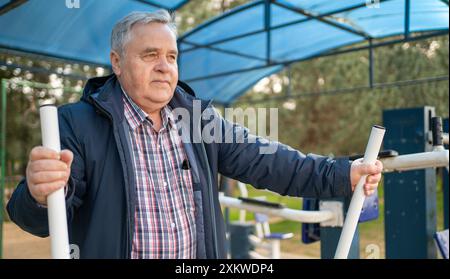 Uomo anziano che fa esercizi di fitness in attrezzature di allenamento pubbliche. Stile di vita attivo e sport in età avanzata. Foto Stock