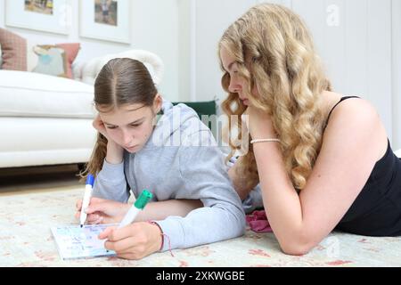 Due ragazze che fanno matematica sdraiate sul pavimento scrivono su lavagna bianca con penne frazioni di algebra sorelle di matematica ragazze di educazione matematica in STEM Foto Stock