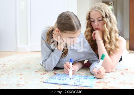 Due ragazze che fanno matematica sdraiate sul pavimento scrivono su lavagna bianca con penne frazioni di algebra sorelle di matematica ragazze di educazione matematica in STEM Foto Stock