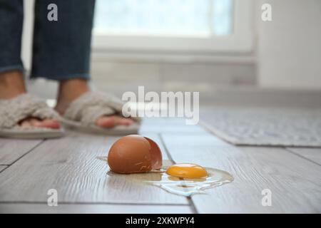 Donna vicina a un uovo crudo rotto su un pavimento in legno grigio in interni, messa a fuoco selettiva. Spazio per il testo Foto Stock