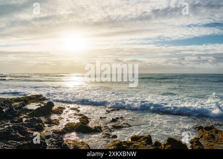 Un bellissimo tramonto su una spiaggia rocciosa con onde che si infrangono Foto Stock