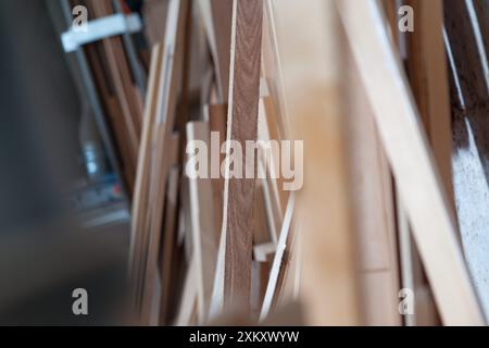 Tavole e tavole di legno si appoggiano a una parete in un'affollata officina di falegnameria, mettendo in mostra la maestria artigianale con tonalità calde e dettagli complessi Foto Stock