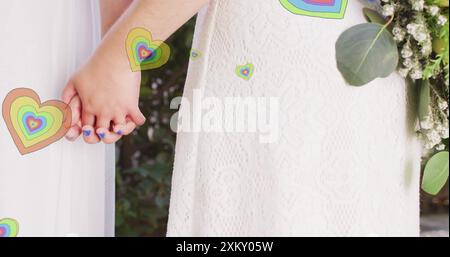 Immagine di cuori che fluttuano sopra diverse coppie sposate che si tengono per mano Foto Stock