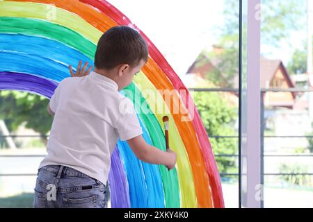 Bambino che disegna l'arcobaleno su una finestra all'interno Foto Stock