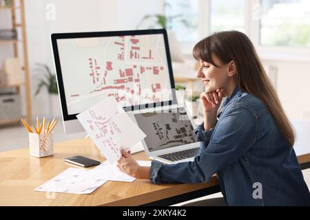 Cartografo sorridente che lavora con le mappe catastali al tavolo in ufficio Foto Stock