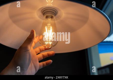 Le mani di una donna cambiano la lampadina. Una mano che cerca le lampadine concettuali. Primo piano delle mani femminili che installano una lampadina eco. Foto Stock