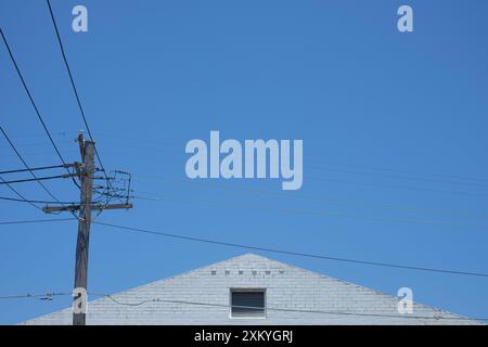 Triangolo bianco di muratura contro un cielo australiano azzurro, a sinistra un polo elettrico grigio asciutto attraversato da linee elettriche aeree Foto Stock