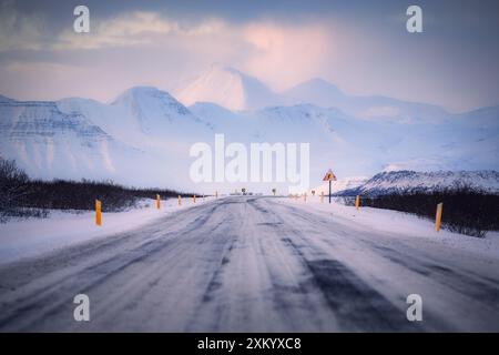 La circonvallazione islandese Route 1, durante l'inverno, in una bella serata di sole, con montagne sullo sfondo, asfalto ricoperto di neve, desolato, sconosciuto Foto Stock