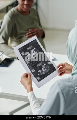 Ecografia del feto su carta in mani di medico femminile seduto sul posto di lavoro in ufficio medico e discutere i risultati dell'ecografia con il paziente Foto Stock