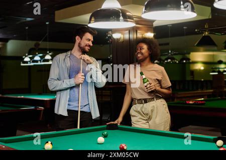 Felice giovane coppia interculturale che si guardano l'un l'altro e chiacchierano davanti al tavolo da biliardo prima o dopo la partita a biliardo Foto Stock
