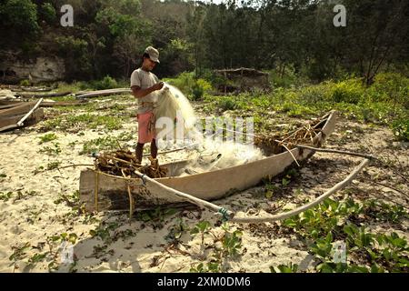 Un pescatore di sussistenza che srotola la sua rete di pesca sulla spiaggia di Tarimbang a Tabundung, Sumba orientale, Nusa Tenggara orientale, Indonesia. Foto Stock