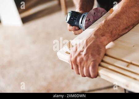 Carpenter sta levigando una tavola di legno utilizzando una levigatrice orbitale nella sua officina, dimostrando la sua abilità e competenza nella lavorazione del legno Foto Stock