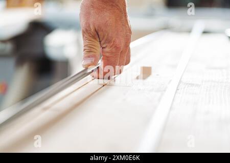 Carpenter utilizza con cura uno scalpello per modellare una tavola di legno nella sua officina, dimostrando precisione e maestria artigianale Foto Stock