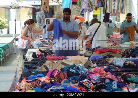 Parma, Italia 24 luglio 2024 i clienti che navigano e acquistano abbigliamento e tessuti in un mercato all'aperto con un venditore ambulante che mostra un capo blu Foto Stock