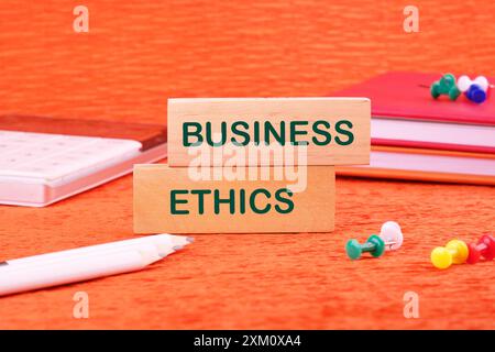 concetto di termini aziendali. Etica aziendale, testo scritto su blocchi di legno davanti a uno sfondo arancione Foto Stock