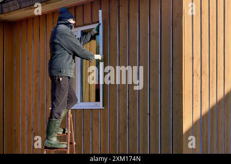 In piedi sulla scala a cavalletto, l'appaltatore di tetti installa le pendenze metalliche delle finestre sul lato della facciata. Foto Stock