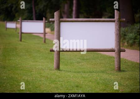 insegna bianca vuota con pali di legno e cornice sull'erba a lato di un piccolo viale rettilineo con foresta e alberi sullo sfondo Foto Stock