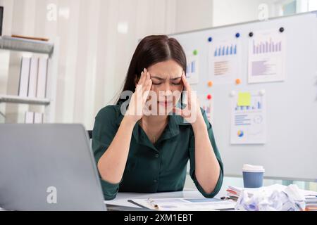 Donna d'affari stressata alla scrivania con notebook e documenti, che soffre di stress e fatica sul lavoro Foto Stock