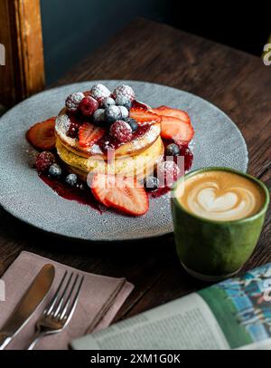 Soffice pancake fatto in casa con frutta e marmellata sulla parte superiore con una tazza di cappuccino. Foto Stock