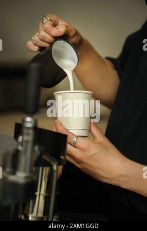 Mani maschili che versano latte e preparano cappuccino fresco. Artista del caffè. Foto Stock