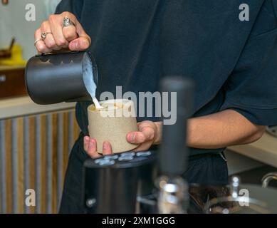 Mani maschili che versano latte e preparano cappuccino fresco. Artista del caffè. Foto Stock