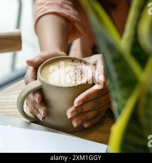Mani di donna che tengono una tazza di caffè sul tavolo di legno. Foto Stock