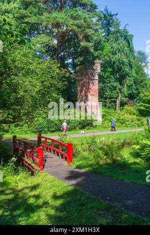 Upper Gardens, Bournemouth, UK - 10 luglio 2024: Passerella rossa che attraversa il Bourne Stream di fronte alla Bournemouth Gardens Water Tower. Foto Stock