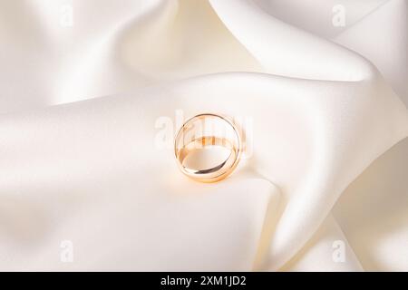 Due eleganti fedi nuziali dorate si trovano su morbide pieghe in raso beige. elegante sfondo per matrimoni. cartolina. invito. Presentazione del prodotto Foto Stock