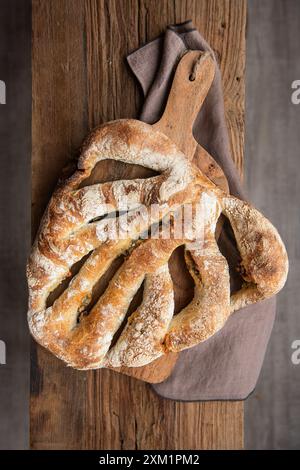 Formaggio a pasta madre e pane alle olive. Pane di frumento biologico appena sfornato su un tagliere su un banco di legno, con tovaglia di lino. Vista dall'alto Foto Stock