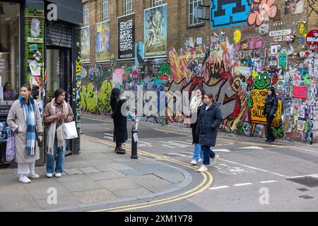 I pedoni camminano di fronte alle pareti coperte di graffiti, Londra Foto Stock