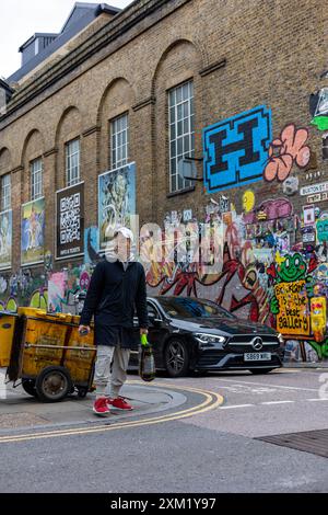 Pedonale con scarpe da ginnastica rosse e Mercedes nera da un muro coperto di graffiti, Londra Foto Stock