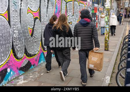 Gli adolescenti camminano lungo un muro ricoperto di graffiti, Londra Foto Stock