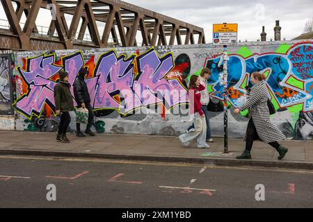 I pedoni camminano di fronte a un muro coperto di graffiti, Londra Foto Stock