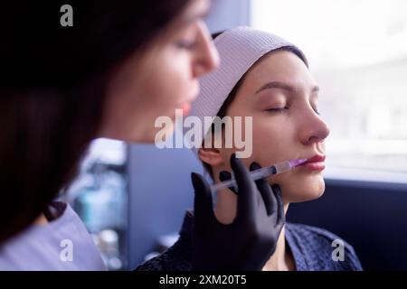 Iniezioni di bellezza. Una cosmetologa donna con guanti neri fa un'iniezione al suo cliente. Trattamento con acido ialuronico. Introduzione di liquido in Foto Stock