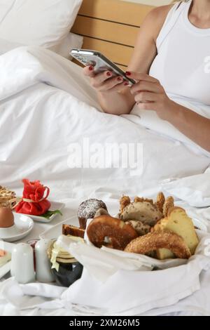 Giovane donna che fa colazione nel letto. Mattinata tranquilla e idilliaca a casa o in camera d'hotel Foto Stock