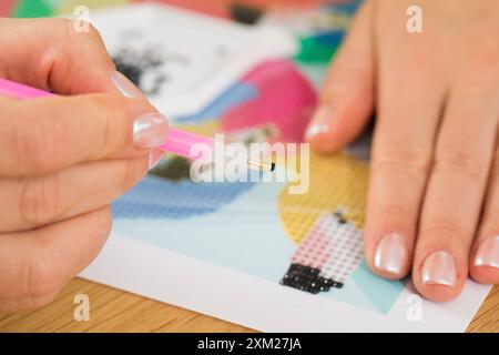 Primo piano di una mano che posiziona cristalli su una tela per un progetto di pittura a diamanti. Mosaico diamantato Foto Stock